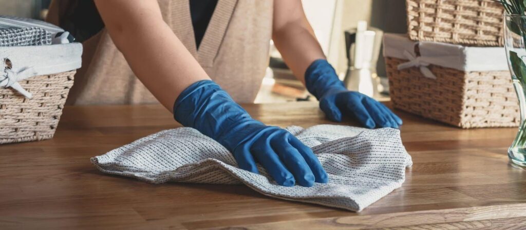 A woman in blue gloves diligently cleans a table, ensuring a spotless and tidy surface