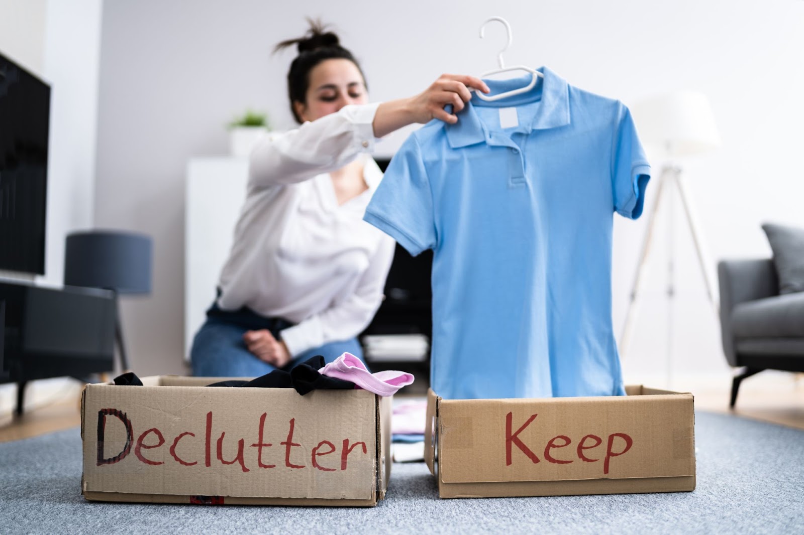 A woman sorting clothes into cardboard boxes labeled Declutter and Keep during a home organization project.