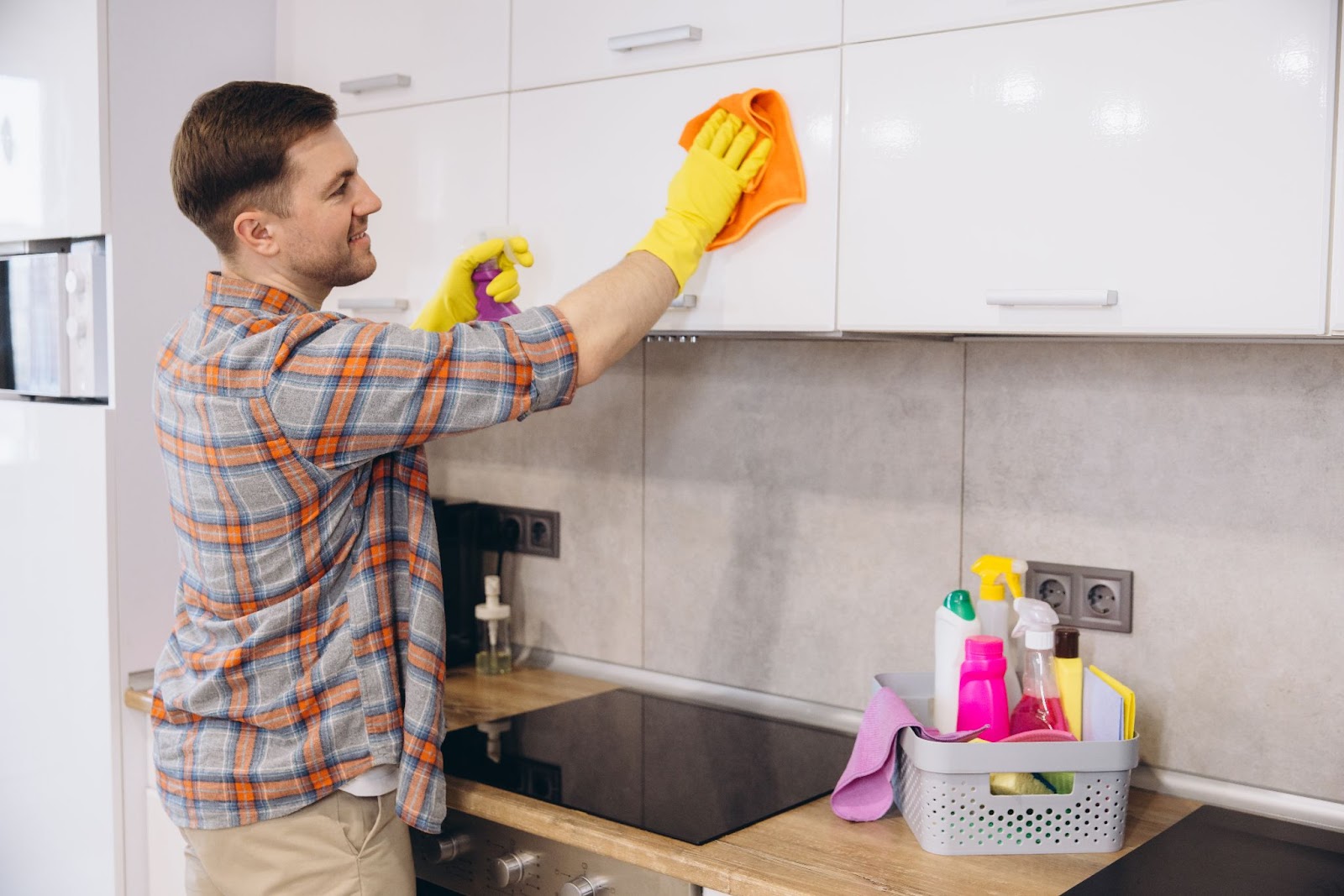 Person in yellow gloves cleaning kitchen cabinets with a cloth and spray.