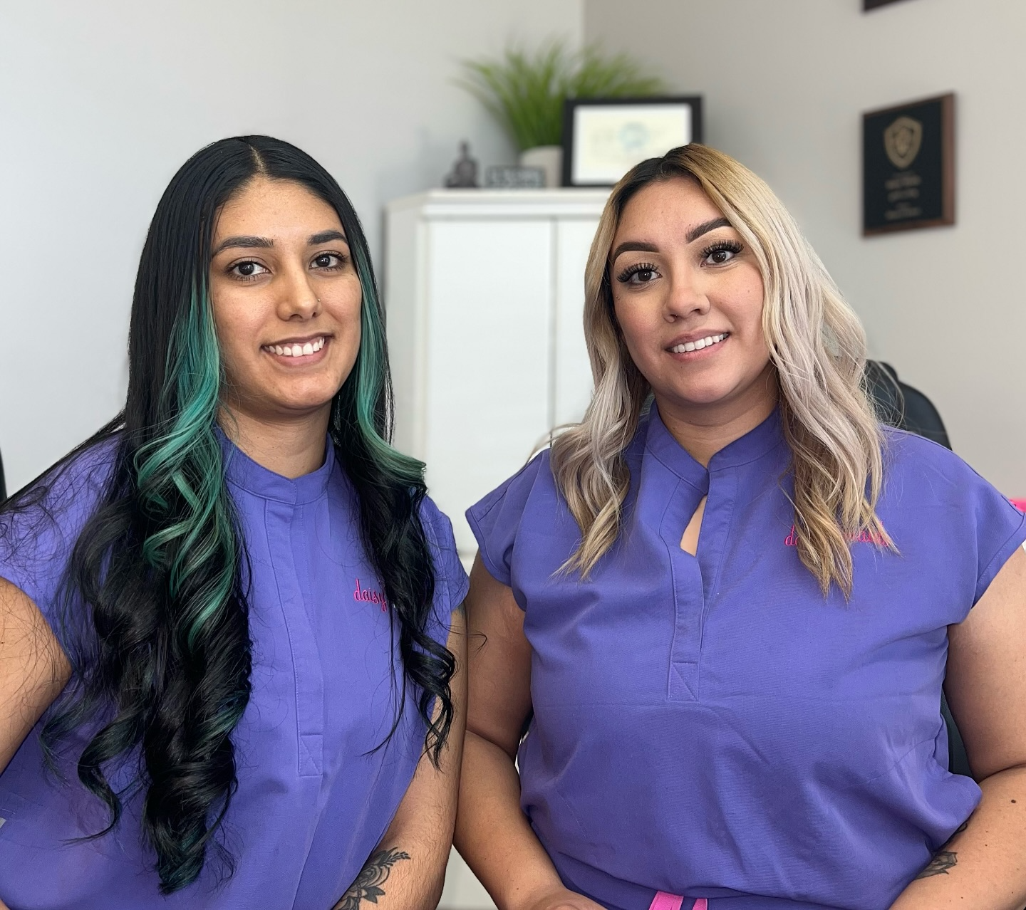 Two women in purple shirts sit side by side, smiling and engaged in conversation.