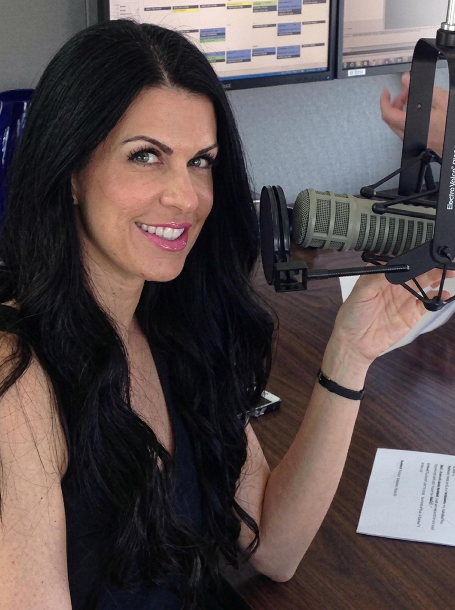 A woman sits in front of a microphone, preparing to speak or perform, with a focused expression on her face.