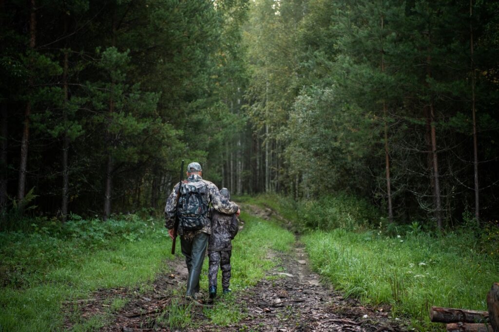 A father and son walk through a vibrant forest, ready for their guided hunt in the great outdoors.