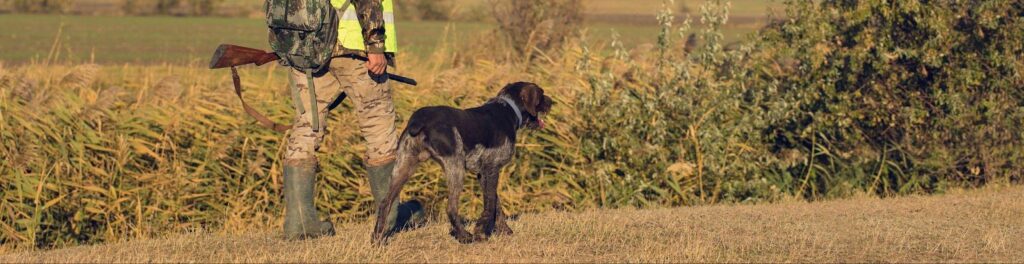 A man holding a gun with a dog by his side, standing next to a pole