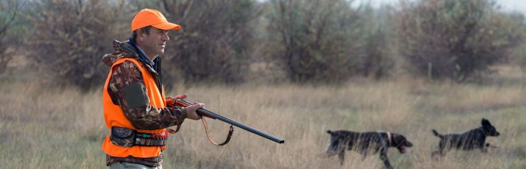 A man in an orange vest and hat holding a gun. Guided hunts, elk hunting, and hunting company.