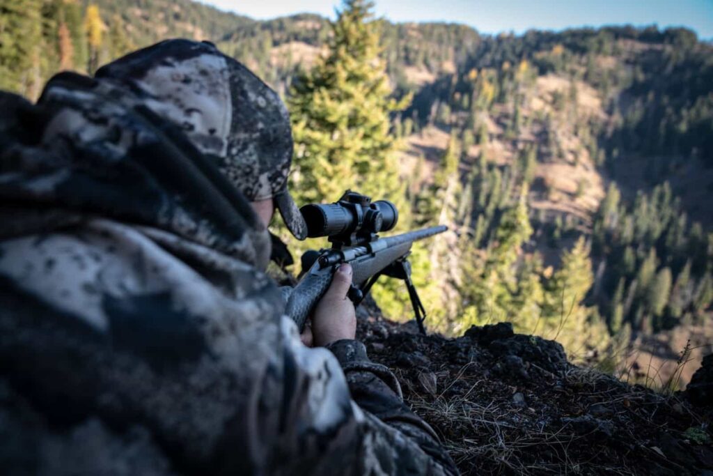 A man in camouflage gear aims a rifle during a guided hunt trip offered by a hunting company.