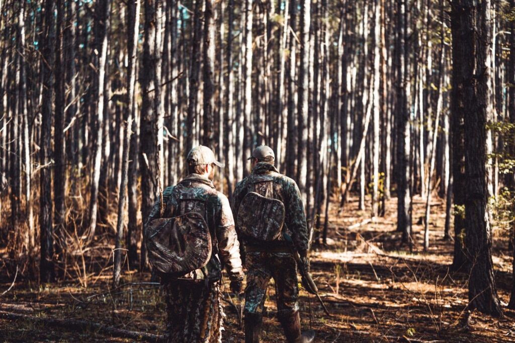 Two men in camouflage trek through a dense forest
