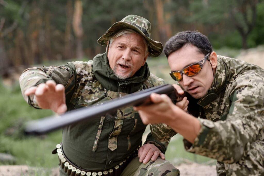 Two men in military camouflage, directing a firearm, indicating a serious engagement in a wooded area