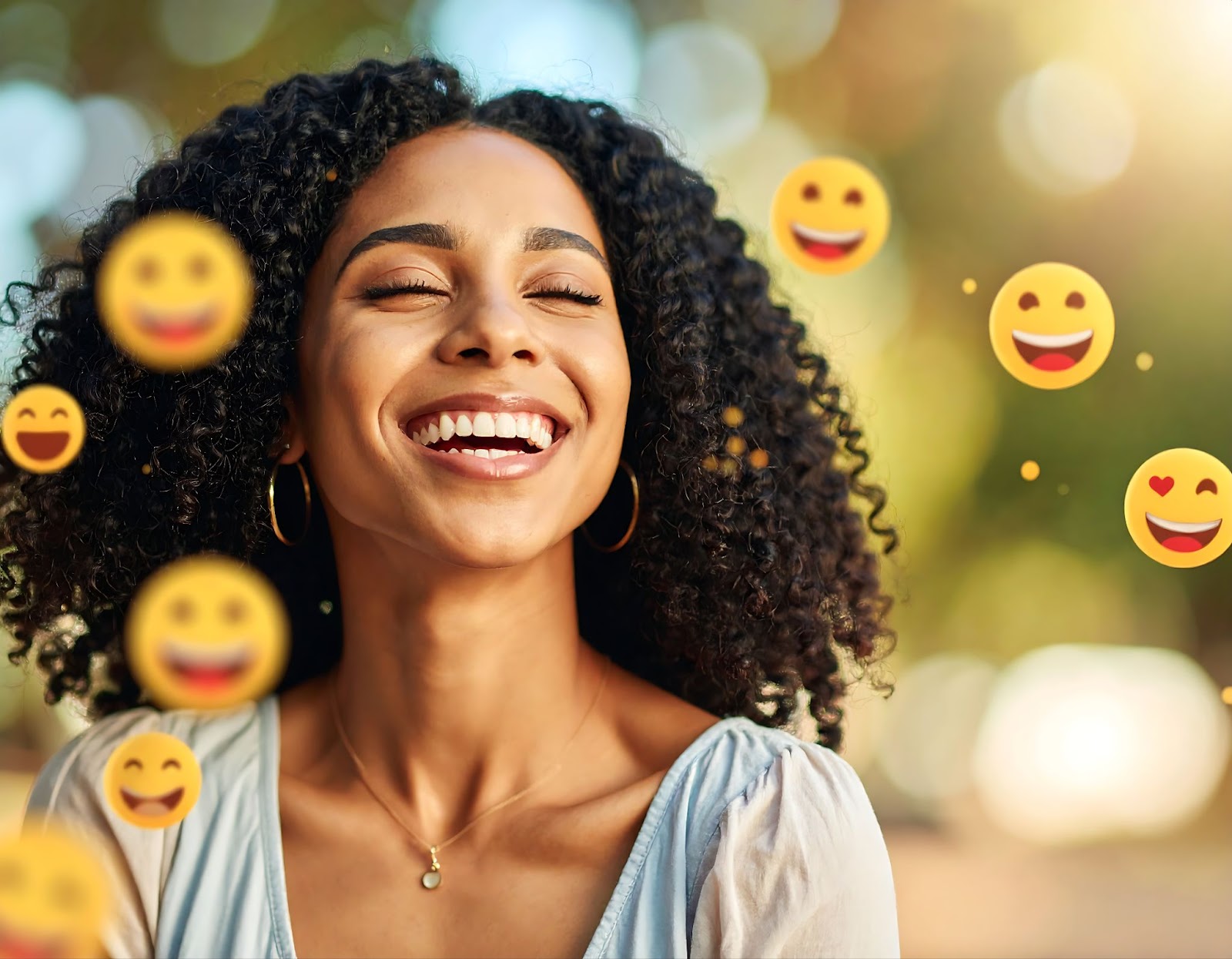 A joyful woman with curly hair surrounded by floating smiley emojis in a bright outdoor setting.