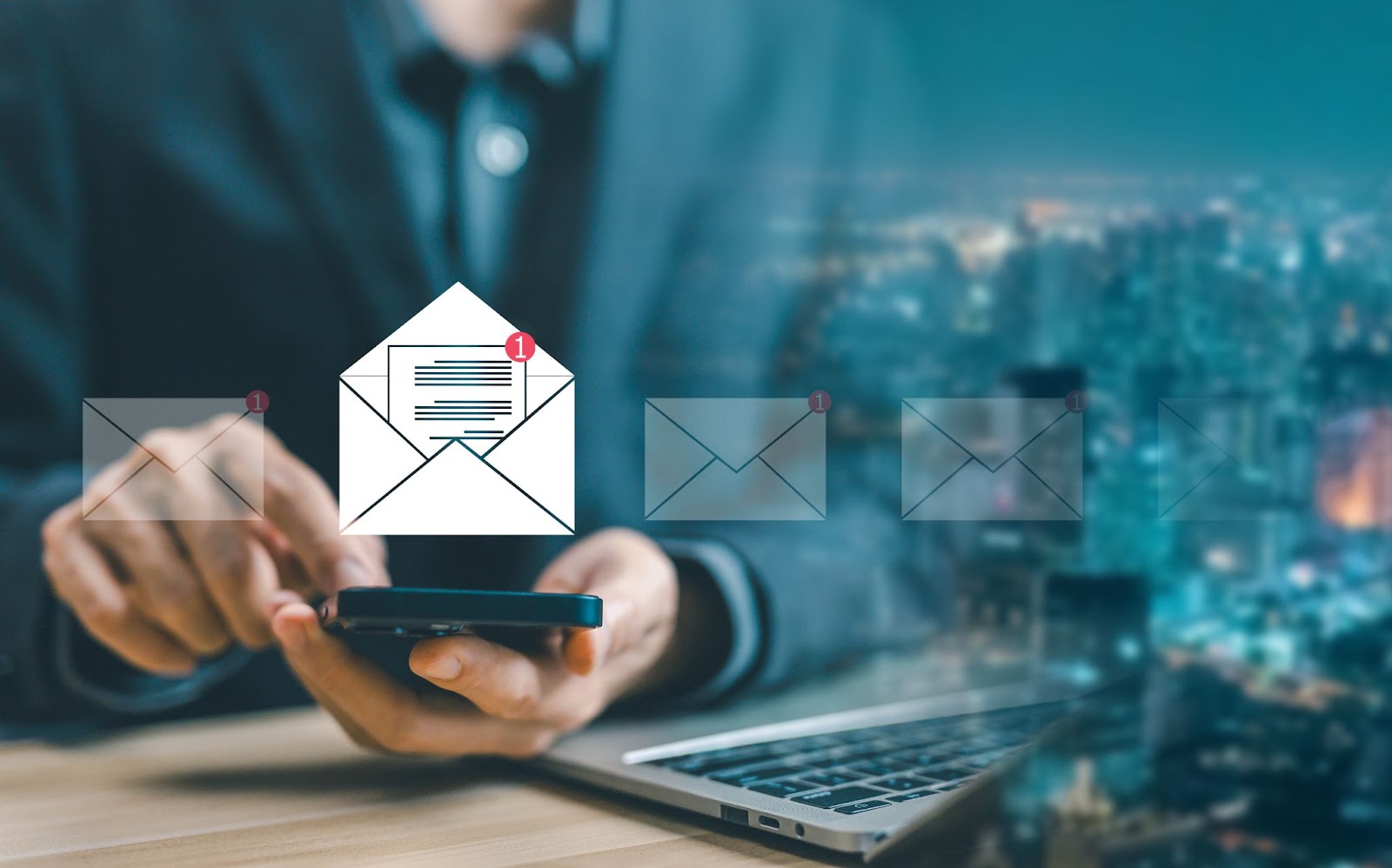 A person holding a smartphone with email icons and notifications over a laptop on a desk, with a blurred cityscape background.