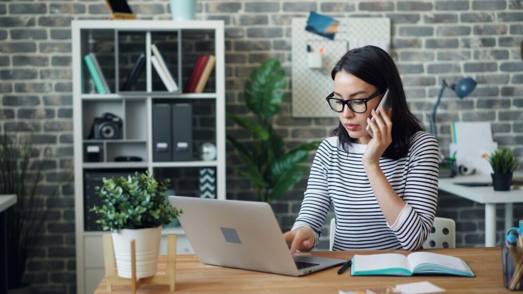A woman wearing glasses is seated at a desk, working on a laptop in a Utah marketing agency setting.