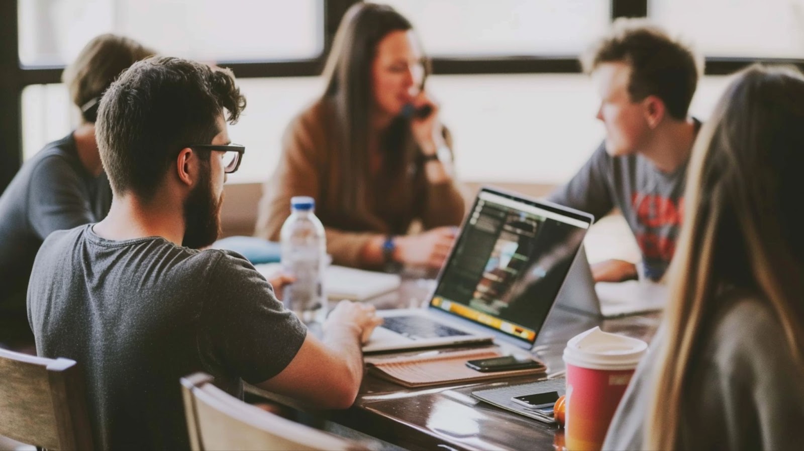 Group of people collaborating around a table with laptops and coffee in a cafe setting.